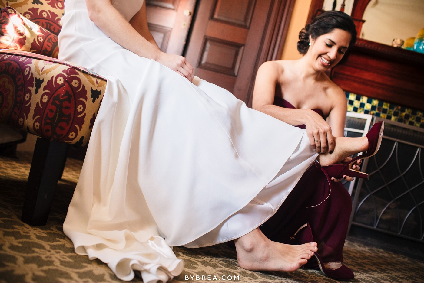 Bride sitting while bridesmaid puts red shoe on for her